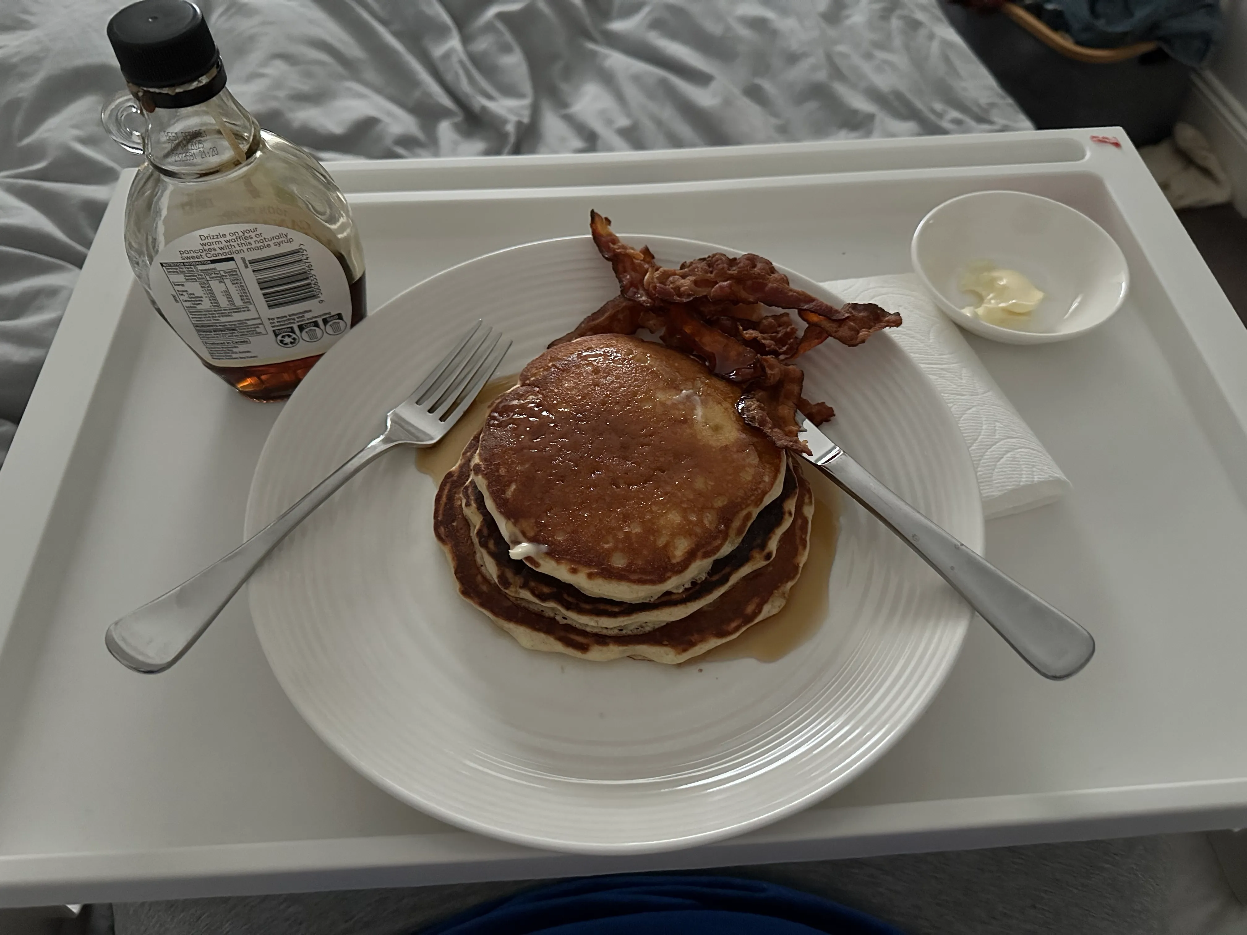 Pancakes and bacon on a tray in bed