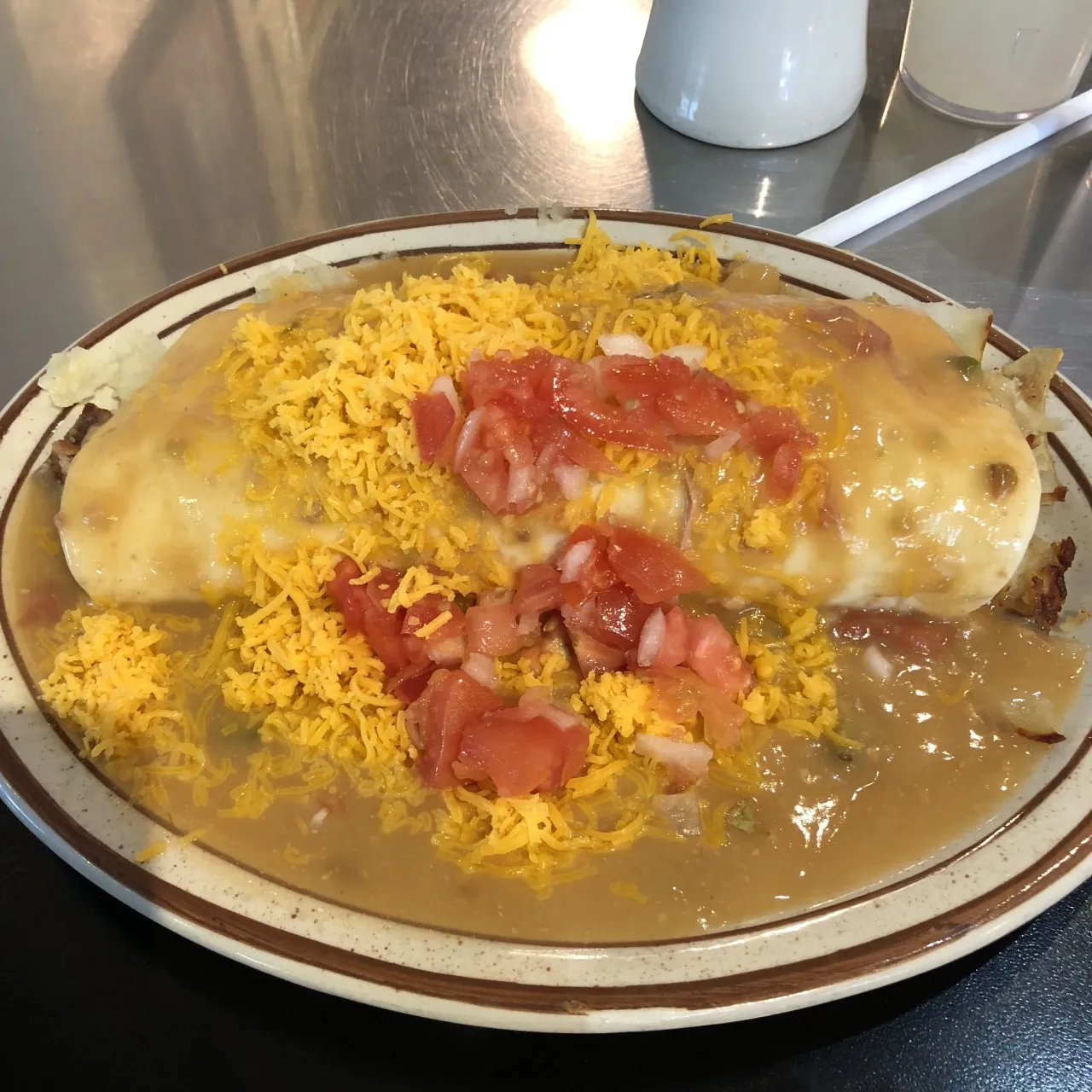 A breakfast burrito smothered in green chile and topped with cheese